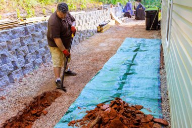 İnşaat alanında, işçiler yeraltındaki delikli borulardan oluşan drenaj sistemi kurmak için siper kazıyorlar..