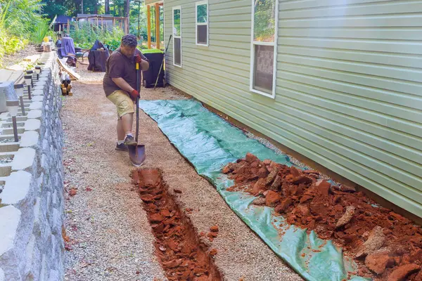 stock image At construction site, worker digs trench for laying drainage system perforated pipe underground.