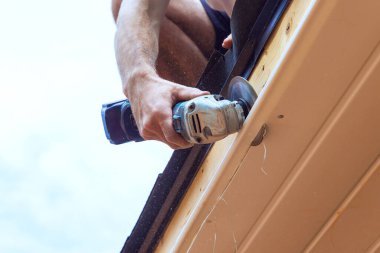 Çalışanlar, yeni evin ön cephesindeki belli boyutlara kadar mevcut vinil soffit plastik panelleri kesiyorlar.