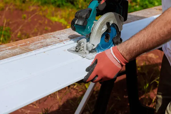 stock image Prior to installing plastic vinyl siding, worker cuts it to size with circular handsaw