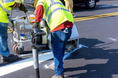 İşçiler, asfalt yerleştirildikten sonra yola işaretler koymak için bir hava fırçası makinesi kullanırlar