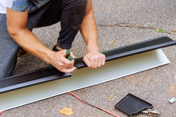 stock image Worker cuts aluminum rain gutters to required size after bending them using machine tool