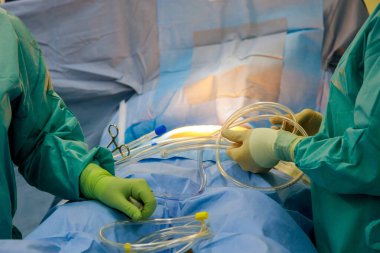 Hasta ameliyattan önce ameliyat masasında yatarken, doktorlar onu ameliyata hazırlıyorlar.