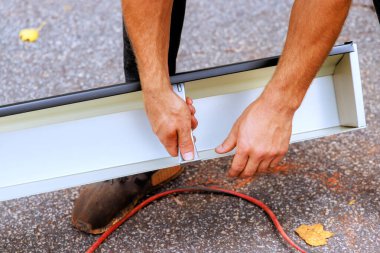 İşçi önceden kurulmuş vidalar kullanarak çatıya yerleştirmeden önce yeni oluklara gizlenmiş oluk askıları ekler