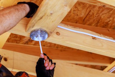 Tavan lambası montajı sırasında bir elektrikçi elektrik kablosunu elektrik kutusuna bağlar