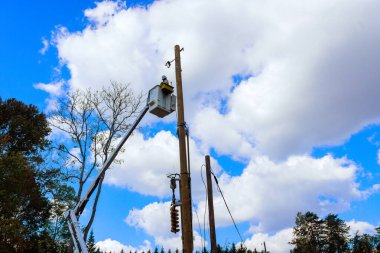 Elektrik hattında çalışan elektrikçi elektrik direklerini tamir ediyor. Kamyon hidrolik kulesi takılı kova kullanarak kasırga üstüne elektrik sistemi kuruyor..