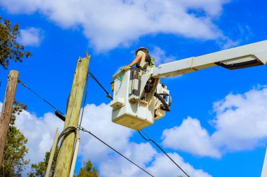 Teknisyen, kasırga üstüne elektrik sistemi üzerinde çalışırken hidrolik kule monte edilmiş kova kullanarak elektrik direğini tamir ediyor..