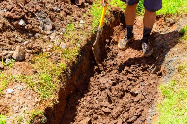 İnşaat alanında, işçiler kanalizasyon boruları için kürekle siper kazıyorlar.