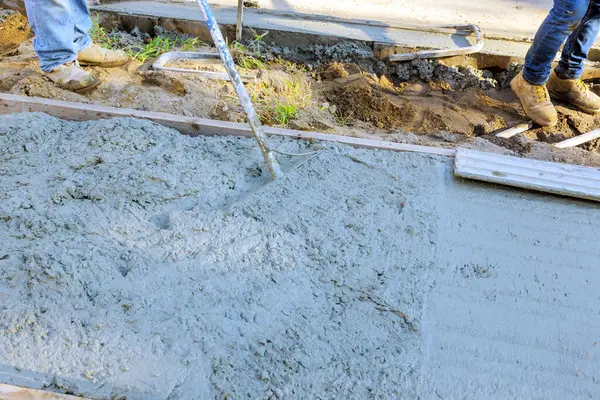 Bir çalışan beton döşemek için mala kullanırken kaldırım yeni çimento dökülüyor.