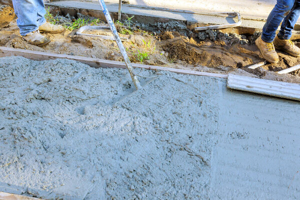Работник использует лопату, чтобы выровнять бетон, в то время как тротуар свежезалитый цементом