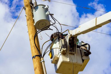 Bucket truck supports worker attending to electrical infrastructure on pole after hurricane clipart