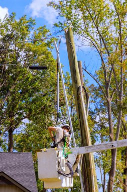 Lineman operates from raised lift to inspect maintain power transformer on a pole after hurricane clipart