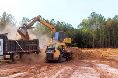 An excavator is used to load earth into dump truck on construction site. clipart