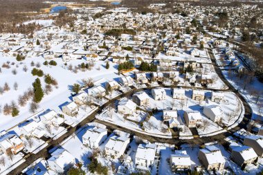 Karlı bir Amerikan banliyö manzarası. Açık binalar, yollar, dağınık ağaçlar var..