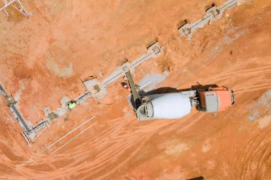Beton karıştırıcı kamyonun kırmızımsı topraklarda temel hattı boyunca taze beton döktüğü inşaat alanının havadan görüntüsü..