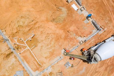 İnşaat işçisi tarafından kullanılan beton karıştırıcı kamyon, kırmızımsı toprakla kaplı bir alana beton döküyor..