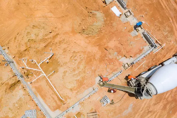 İnşaat işçisi tarafından kullanılan beton karıştırıcı kamyon, kırmızımsı toprakla kaplı bir alana beton döküyor..