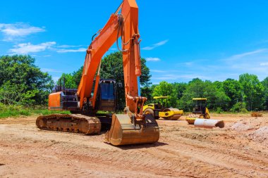 Bir kazıcı toprağı kazarken iki yol silindiri inşaat alanındaki zemin hazırlıyor.