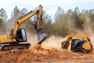 Buldozer kazısı ağır makineler inşaat alanındaki karaları temizlemek için birlikte çalışırlar. Toz bulutları zemini kazar ve yaklaşan gelişime hazırlanırlar..