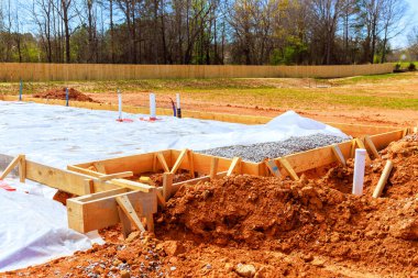 İnşaat sahasında, nemden korunmak için koruyucu plastikle çevrili çakıllarla dolu ahşap formlar hazırlanıyor.