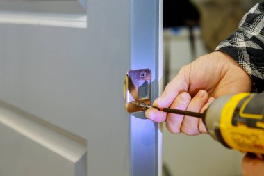 Kapı mandalını tornavida kullanarak kuran işçiler, ayarlar düzenlidir, inşaat sırasında DIY becerileri gösterilir