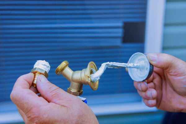 Worker holds brass fitting in one hand applies sealant with tool preparation for plumbing work.