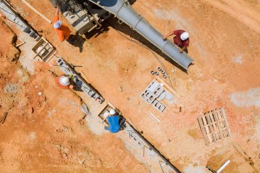 Beton karıştırıcı kamyon geniş, kırmızımsı toprak alanlarına beton dökerken, inşaat işçilerinin betonu kullandıkları gözlemleniyor..