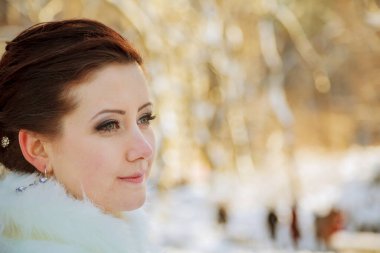 Kahverengi saçlı kadın kışın zarif bir şekilde dışarıda dikiliyor. Sakin ifadesi ağaçların arasından süzülen yumuşak ışıkla vurgulanıyor..