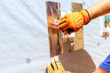 İnşaat alanının duvarına yalıtım malzemesi yerleştirmek için eldiven kullanan işçilerin elleri