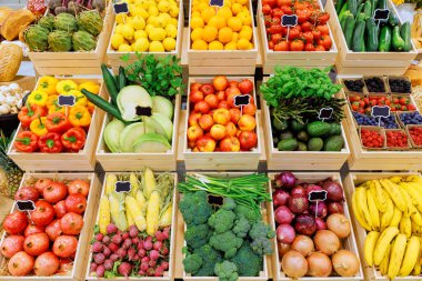 Renkli meyveler, sebzeler sandıkların içinde sergileniyor. Parlak güneş ışığı altında yerel pazarın ödülleri sergileniyor..