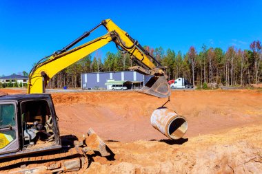 İnşaat alanında ağır makineler çalışıyor, beton boru döşemek için yerden boruları kaldırıyor.