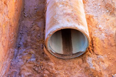 Açığa çıkan beton boru toprak içinde, toprakla çevrili, inşaat alanında çakıl var..