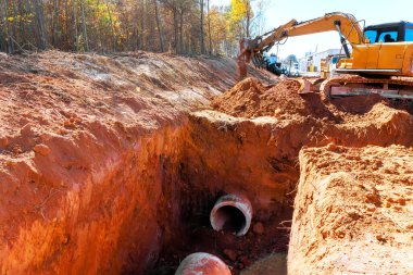 Ağır kazıcılar, konut inşaatıyla çevrili yeni borular için siper kazmaya çalışıyor.