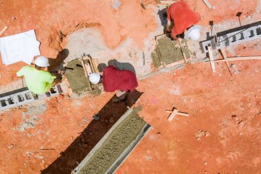 Büyük beton karıştırıcı kamyonu inşaat sahasına yerleştirildi, kahverengi toprak yüzeyine temel destek için zemin seviyesindeki kalıplara beton dökülüyor..