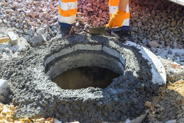 Taze beton, bir yeraltı altyapı çukuru için rögar kapağının üstündeki blokları güvence altına almak için kullanılıyor..