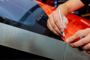 Teknisyen, vücut otomobilini korumak için turuncu vinil filmi arabadan arabaya keserken hassasiyete odaklanıyor.