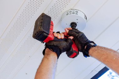 Delik testereli kablosuz matkap kullanarak, eldivenli el, beyaz tavandaki dairesel deliği keserek yeni bir aydınlatma armatürü kuruyor