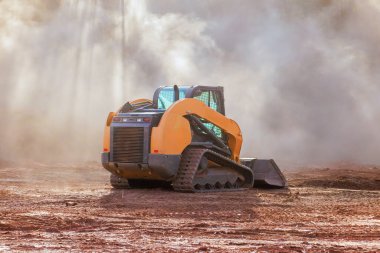 İnşaat alanında kompakt buldozer mekanizması çalışıyor. Toprak taşıma sırasında tozu karıştırmak arazi hazırlama alanı geliştirme çalışmasıdır..