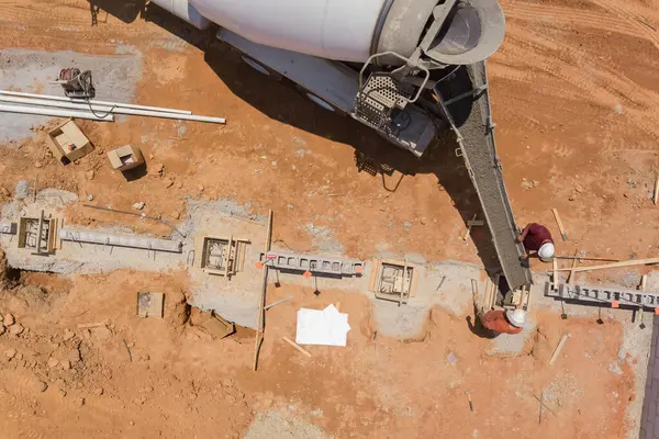 İnşaat işçisi, beton kamyonu kirmizi toprakla çevrili geniş bir alanda temel boyunca beton döküyor..