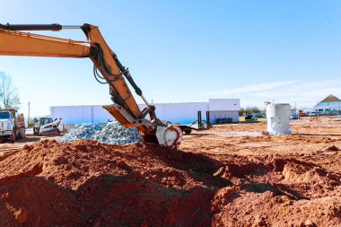İnşaat kazıcısı, drenaj borusunun altındaki inşaat sahasında kırmızı toprağı kazıyor