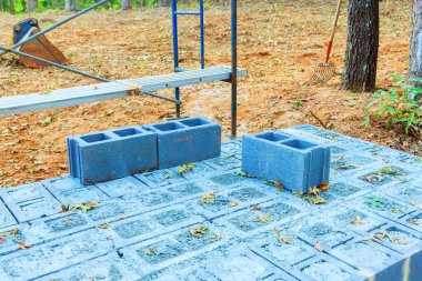 Gray concrete blocks sit on dirt surface in wooded area, indicating construction progress on sunny day. clipart