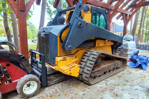 İzlenen yükleyici, inşaat sırasında ağaçlarla çevrili ahşap pavyonun yanında dinleniyor.
