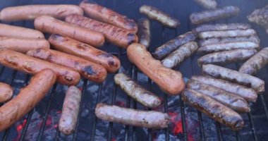 Sosisler ızgarada cızırdıyor, güneşli yaz barbekü kutlaması sırasında dumanlı aromalar yayıyor..