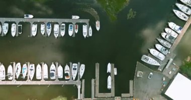 Birçok tekne marinada hizalanır, güneşli gökyüzünün altında sakin sulara yansıyarak insanların günün tadını çıkarırlar..