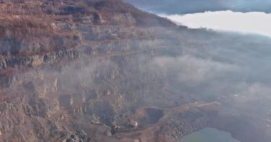 Hava görüntüsü, ağır makineleri sislerle çevrili taş ocağında çalıştırıyor ve hala suyun kayalık arazisini ortaya çıkarıyor..