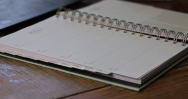 Boş haftalık planlayıcı dizüstü bilgisayarın yanındaki ahşap masaya uzanır. Görev etkinliklerini planlamaya hazırdır..