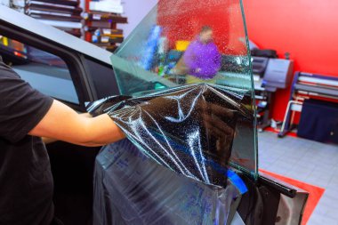 Teknisyen, iyi donanımlı bir oto tamirhanesinde arabanın üzerine dikkatlice renkli film kuruyor..