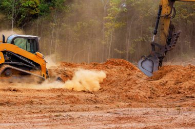 Orman bölgesinde, ağır makineler aktif olarak kara tozu kalıntılarını temizliyor. Toprak, yaklaşan inşaat projelerine hazırlanırken havayı dolduruyor.