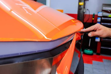 Technician carefully applies orange vinyl wrap to vehicle in an auto shop, for car body protect, ensuring precision quality clipart