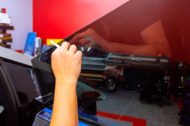 Technician worker carefully installs window tint on car door while working in modern automotive workshop. clipart